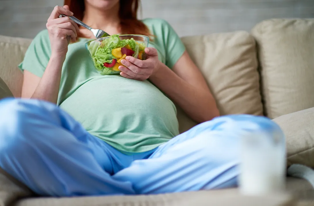 Pregnant woman leaning against a chair's backrest and stroking her bump