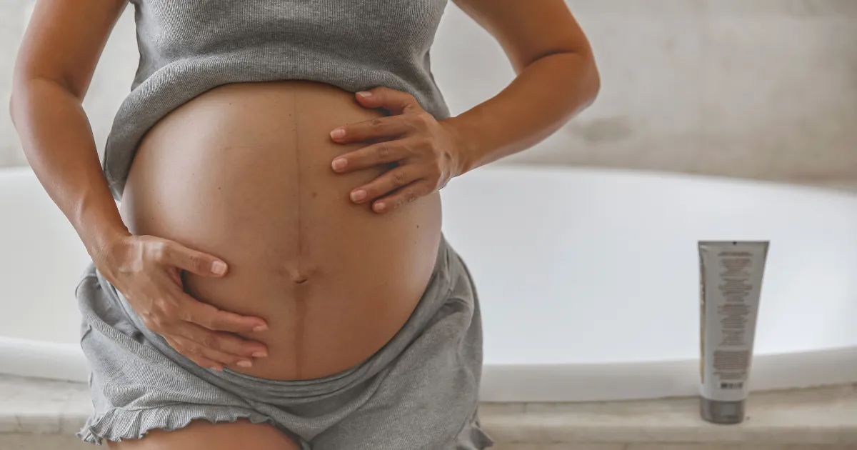 امرأة حامل تضع كريمًا مرطبًا على بشرة بطنها